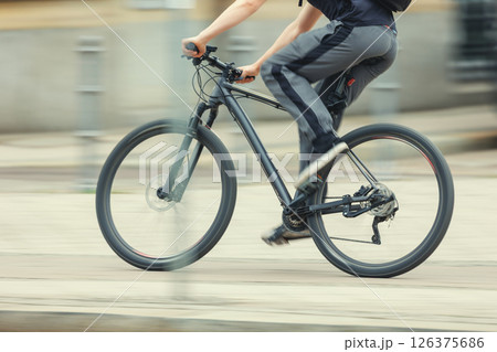 Man in sport suit riding fast black bicycle on European city street dynamic motion blurred background on sunny day. Urban bike commute work ride employee healthy lifestyle eco-friendly transport 126375686