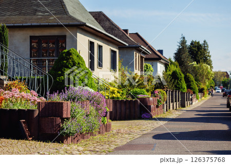 City street of single-family modern houses Germany blooming flowers bed  green bush hedge. German suburban small town residential area row eco sustainable life building neighborhood suburb 126375768