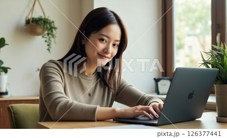 自宅の明るい部屋でノートパソコンを使うカメラ目線の若い女性 126377441