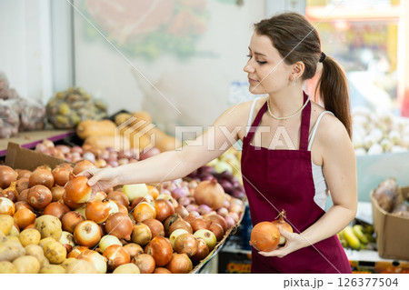 Young woman seller puts onions in vegetable shop Young woman seller puts onions in vegetable shop 126377504