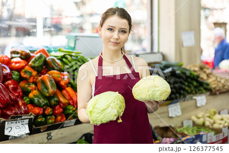 Grocery store female employee places ripe cabbage on a display case at supermarket Grocery store female employee places ripe cabbage on a display case at supermarket 126377545