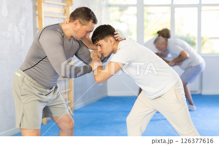 Man ang guy practicing judo techniques in gym with sparring partner, in background men are sparring Man ang guy practicing judo techniques in gym with sparring partner, in background men are sparring 126377616