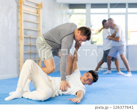 Concentrated man and guy in sport club during training, sparring and practicing technique of hand grab lying down 126377641