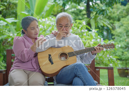 Asian senior couple elderly man playing guitar while his wife singing together outdoors at house, Activity family health care, Enjoying lifestyle during retirement life having fun of senior older Asian senior couple elderly man playing guitar while his wife singing together outdoors at house, Activity family health care, Enjoying lifestyle during retirement life having fun of senior older 126378045