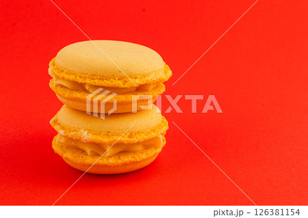 Delicious yellow macarons stacked on a vibrant red background Delicious yellow macarons stacked on a vibrant red background 126381154