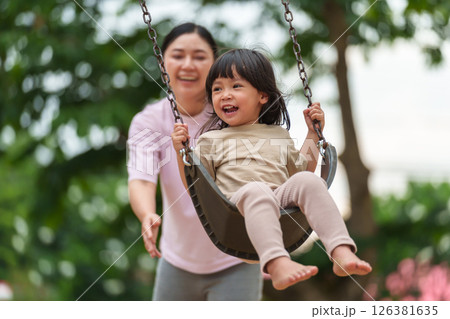 cheerful toddler girl with mother playing on a swing at playground 126381635