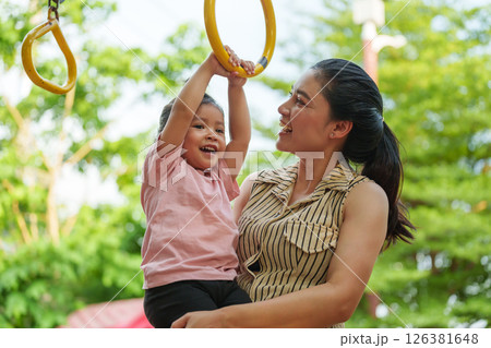 mother holding her daughter to hanging on playground rings in park mother holding her daughter to hanging on playground rings in park 126381648