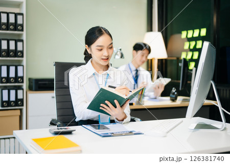 Asian female office worker business suits smiling at camera with working notepad, tablet and laptop documents 126381740