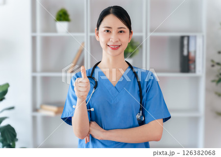 Female doctor or nurse standing and giving thumbs up gesture with stethoscope hanging on her neck. Female doctor or nurse standing and giving thumbs up gesture with stethoscope hanging on her neck. 126382068
