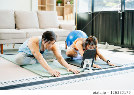 Fitness duo high fiving during an energetic workout session at home, featuring yoga mats, gym equipment 126383179