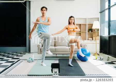 Fitness duo high fiving during an energetic workout session at home, featuring yoga mats, gym equipment 126383203