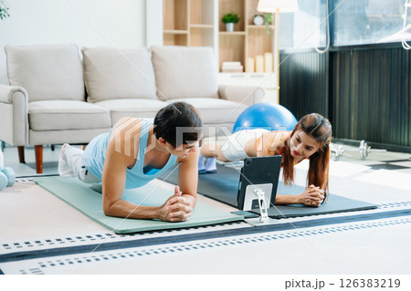 Fitness duo high fiving during an energetic workout session at home, featuring yoga mats, gym equipment 126383219