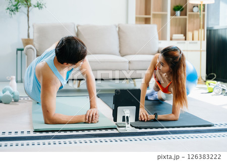 Fitness duo high fiving during an energetic workout session at home, featuring yoga mats, gym equipment Fitness duo high fiving during an energetic workout session at home, featuring yoga mats, gym equipment 126383222