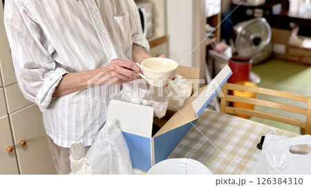 断捨離中にカップを箱から出す高齢女性の手と部屋背景 断捨離中にカップを箱から出す高齢女性の手と部屋背景 126384310