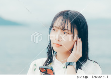 穏やかな海を背景にスマートフォンを操作する若い女性 穏やかな海を背景にスマートフォンを操作する若い女性 126384501