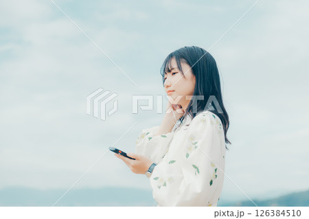 穏やかな海を背景にスマートフォンを操作する若い女性 126384510