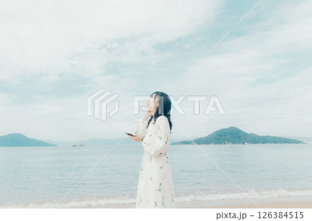 穏やかな海を背景にスマートフォンを操作する若い女性 穏やかな海を背景にスマートフォンを操作する若い女性 126384515