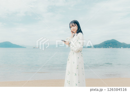 穏やかな海を背景にスマートフォンを操作する若い女性 穏やかな海を背景にスマートフォンを操作する若い女性 126384516
