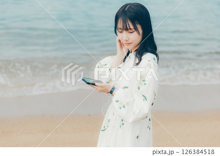 穏やかな海を背景にスマートフォンを操作する若い女性 126384518