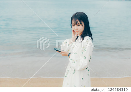 穏やかな海を背景にスマートフォンを操作する若い女性 126384519