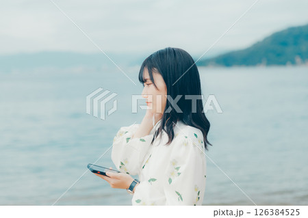 穏やかな海を背景にスマートフォンを操作する若い女性 126384525