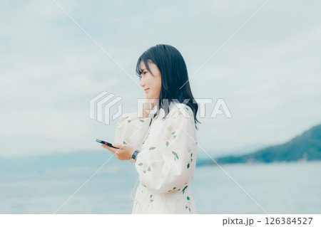 穏やかな海を背景にスマートフォンを操作する若い女性 126384527