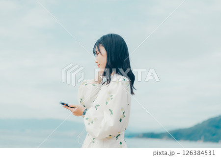 穏やかな海を背景にスマートフォンを操作する若い女性 穏やかな海を背景にスマートフォンを操作する若い女性 126384531