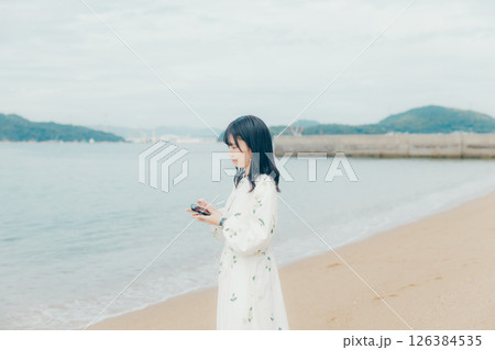 穏やかな海を背景にスマートフォンを操作する若い女性 126384535