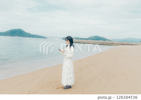 穏やかな海を背景にスマートフォンを操作する若い女性 穏やかな海を背景にスマートフォンを操作する若い女性 126384536
