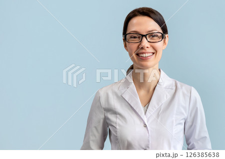 Female doctor in lab coat smiling against blue wall background 126385638