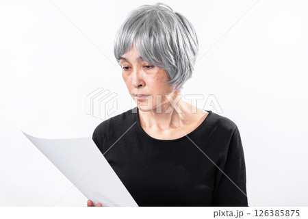 悲しそうに書類を見るシニア女性 悲しそうに書類を見るシニア女性 126385875