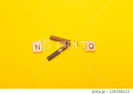 Top view of broken cigarette with the word no on a yellow background closeup Top view of broken cigarette with the word no on a yellow background closeup 126386222