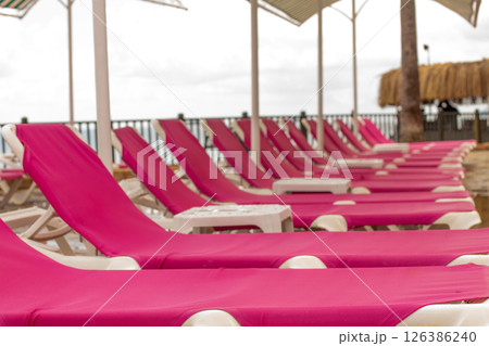 A row of pink deck chairs standing near hotel swimming pool. A row of pink deck chairs standing near hotel swimming pool. 126386240