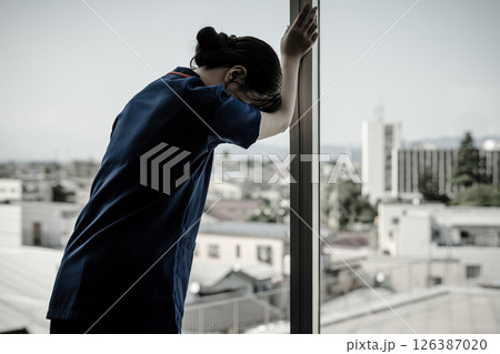 病院の窓を叩いて悔しがる医師・医者・看護師・医療従事者・技師の女性 病院の窓を叩いて悔しがる医師・医者・看護師・医療従事者・技師の女性 126387020