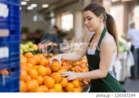 Working in supermarket - female salesman sorts through ripe tangerines on display case Working in supermarket - female salesman sorts through ripe tangerines on display case 126387294