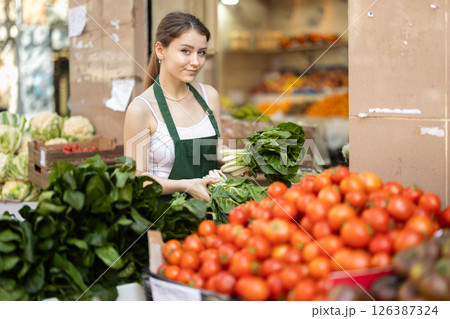 Young woman seller puts spinach in vegetable shop 126387324