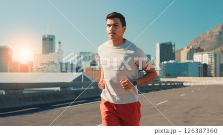 Man, fitness and running in city street for workout, cardio exercise or outdoor training. Active, male person or runner with lens flare on road for physical activity, health or wellness in urban town 126387360