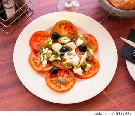 Caprese salad of mozzarella and tomatoes with pesto and olives Caprese salad of mozzarella and tomatoes with pesto and olives 126387435