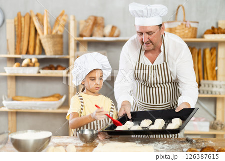 Daughter helps father baker to make pastries, lubricate croissants with loosened egg 126387615