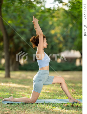 Slim woman practicing yoga - virabhadrasana pose in summer park Slim woman practicing yoga - virabhadrasana pose in summer park 126387781
