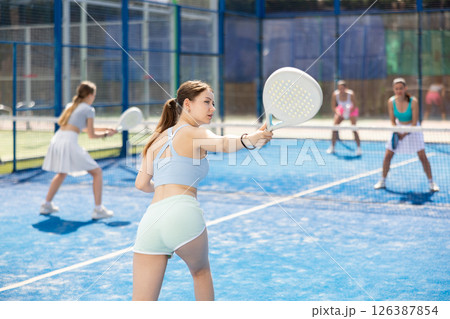 Young woman playing paddle tennis against team of women Young woman playing paddle tennis against team of women 126387854
