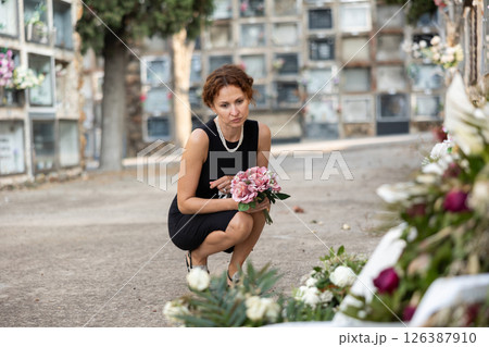 Woman in black dress came to cemetery to lay flowers on grave Woman in black dress came to cemetery to lay flowers on grave 126387910