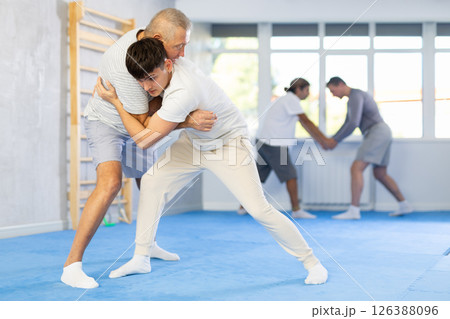 Guy and senior man athletes in pair conduct training battle in oriental fighting technique Guy and senior man athletes in pair conduct training battle in oriental fighting technique 126388096