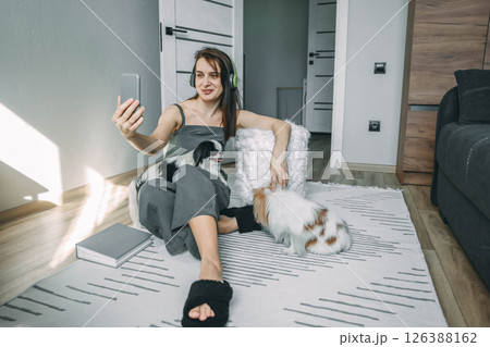 young woman taking a selfie with her dogs, relaxing on the floor in a sunlit apartment, enjoying leisure time at home young woman taking a selfie with her dogs, relaxing on the floor in a sunlit apartment, enjoying leisure time at home 126388162