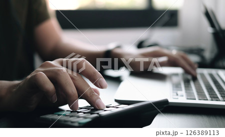 Close up Businessman using calculator and laptop for do math finance on wooden desk in office and business working background, tax, accounting, statistics and analytic research concept 126389113