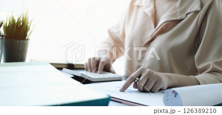 Close up Business woman using calculator and laptop for do math finance on wooden desk in office and business working background tax accounting statistics and analytic research concept 126389210