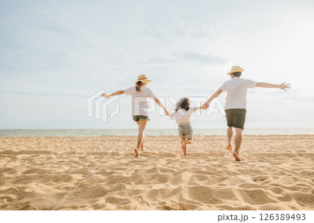 Happy Asian parents with their daughters enjoying playful at beach. Little girls with their mother and father holding hand of child running and pretending on sand. Positive family outdoor activity 126389493