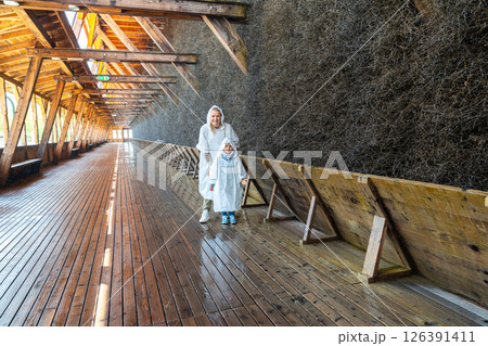 Two people wearing raincoats explore a wooden salt graduation tower. The structure's wooden beams and walls create an atmospheric scene, highlighting architectural details Two people wearing raincoats explore a wooden salt graduation tower. The structure's wooden beams and walls create an atmospheric scene, highlighting architectural details 126391411