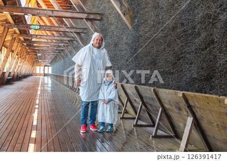 Father and child wearing protective capes in a traditional salt graduation tower. They are smiling and enjoying the experience, surrounded by the unique wooden structure. Father and child wearing protective capes in a traditional salt graduation tower. They are smiling and enjoying the experience, surrounded by the unique wooden structure. 126391417