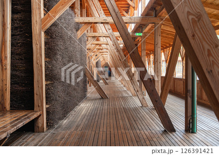 Wooden architectural interior with large beams and natural materials creating a unique passageway. A person stands in the background, adding scale to the geometric design. Salt Graduation Tower 126391421